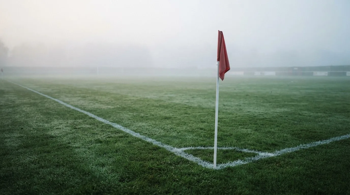 Der Rand eines Spielfelds mit weißer Linie und Eckfahne bei Nebel am frühen Morgen, ohne Menschen.