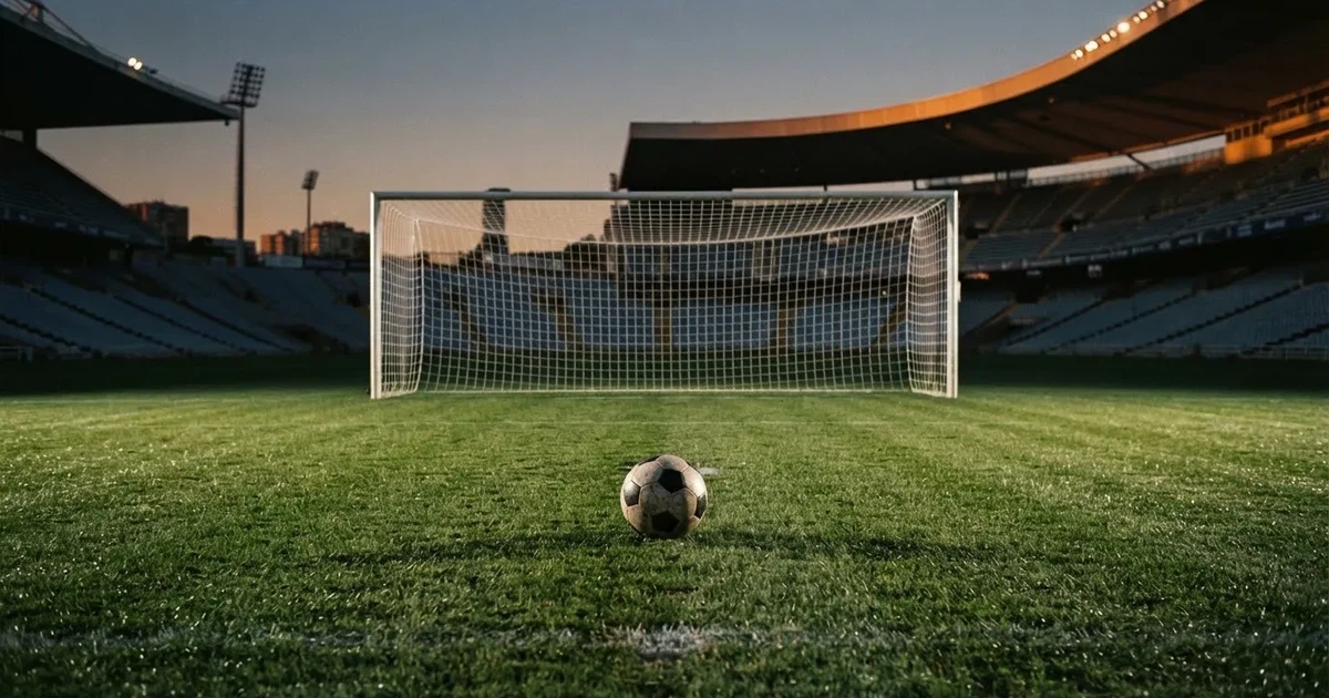 Ein Fußball liegt im Strafraum direkt vor dem Tor mit Netz, im Hintergrund leere Ränge bei Dämmerung.