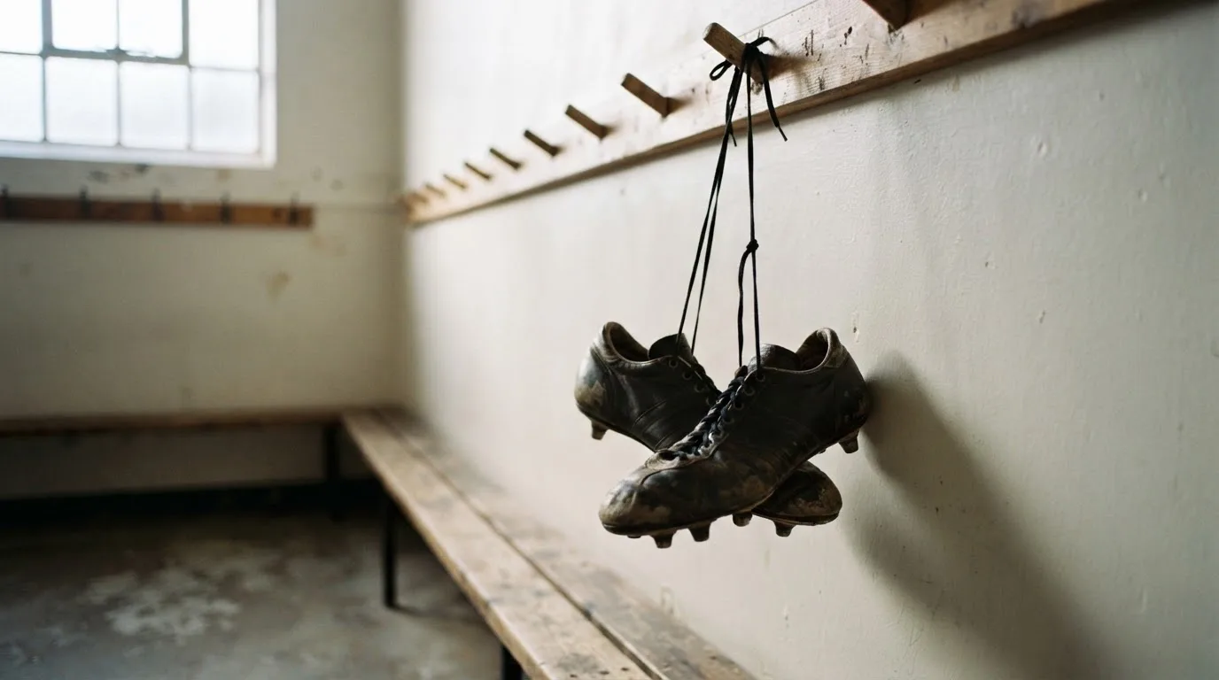 Ein Paar Fußballschuhe hängt an den Schnürsenkeln an einem Holzhaken in einer leeren Umkleidekabine.