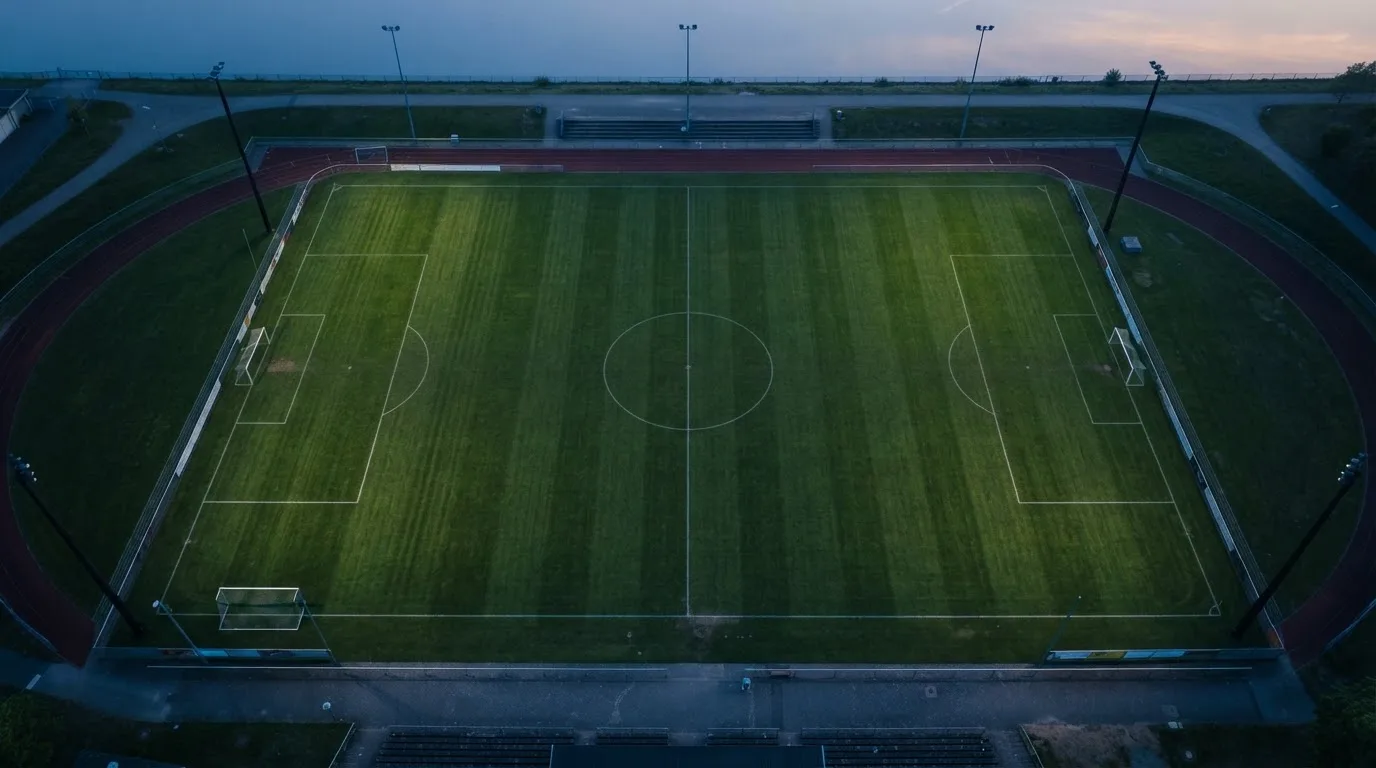 Ein Fußballplatz am Abend aus der Vogelperspektive, Flutlichtmasten ausgeschaltet, die Rasenlinien deutlich sichtbar.