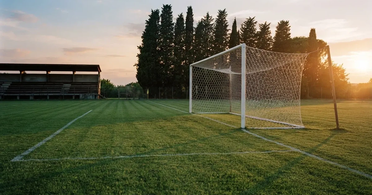 Ein Fußballtor mit Netz auf einem leeren Platz im Abendlicht, der Rasen frisch gemäht, im Hintergrund Zypressen.