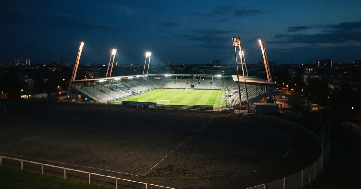 Ein Stadion bei Nacht unter Flutlicht aus der Ferne gesehen, der Rasen ist hell erleuchtet, keine erkennbaren Personen.