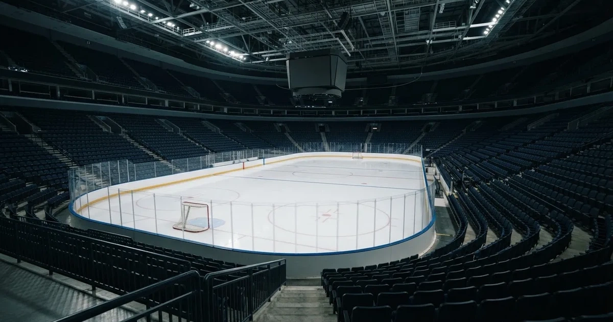 Eine Eishockeyhalle von der Tribüne aus gesehen, spiegelglatte Eisfläche, Banden ohne Schriftzüge, helles Flutlicht.