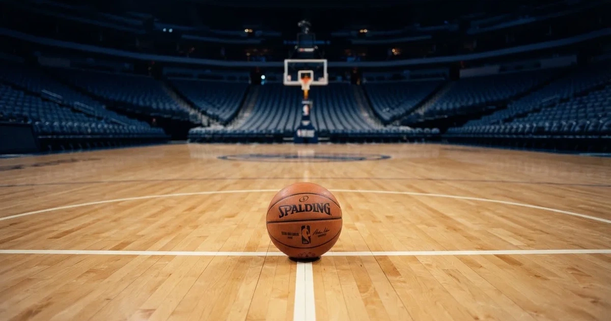 Ein Basketball liegt auf dem Parkettboden einer leeren Arena, Scheinwerfer werfen Licht auf die Mittellinie.