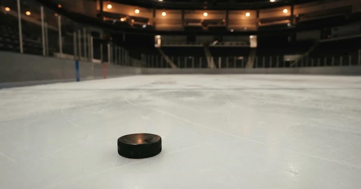 Eine leere Eisfläche in einer Halle mit Banden und Flutlicht, auf dem Eis liegt ein einzelner Puck.