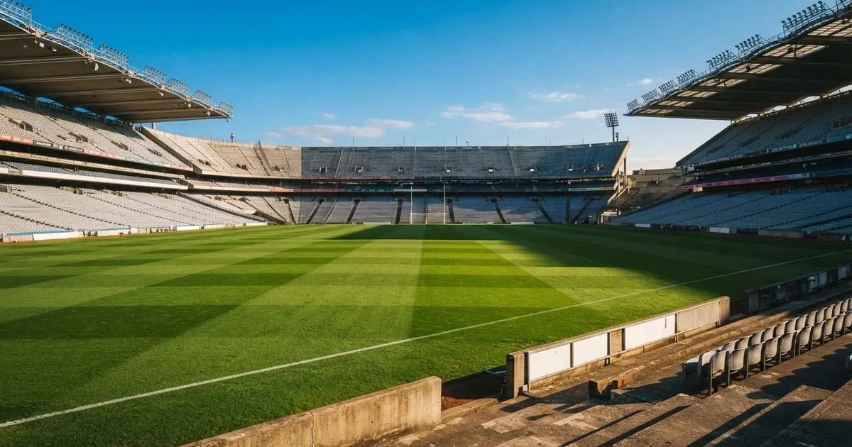 Ein Fußballstadion mit hellen Rängen unter strahlend blauem Himmel, davor ein sonnenbeschienener Rasen mit frisch gemähten Streifen.